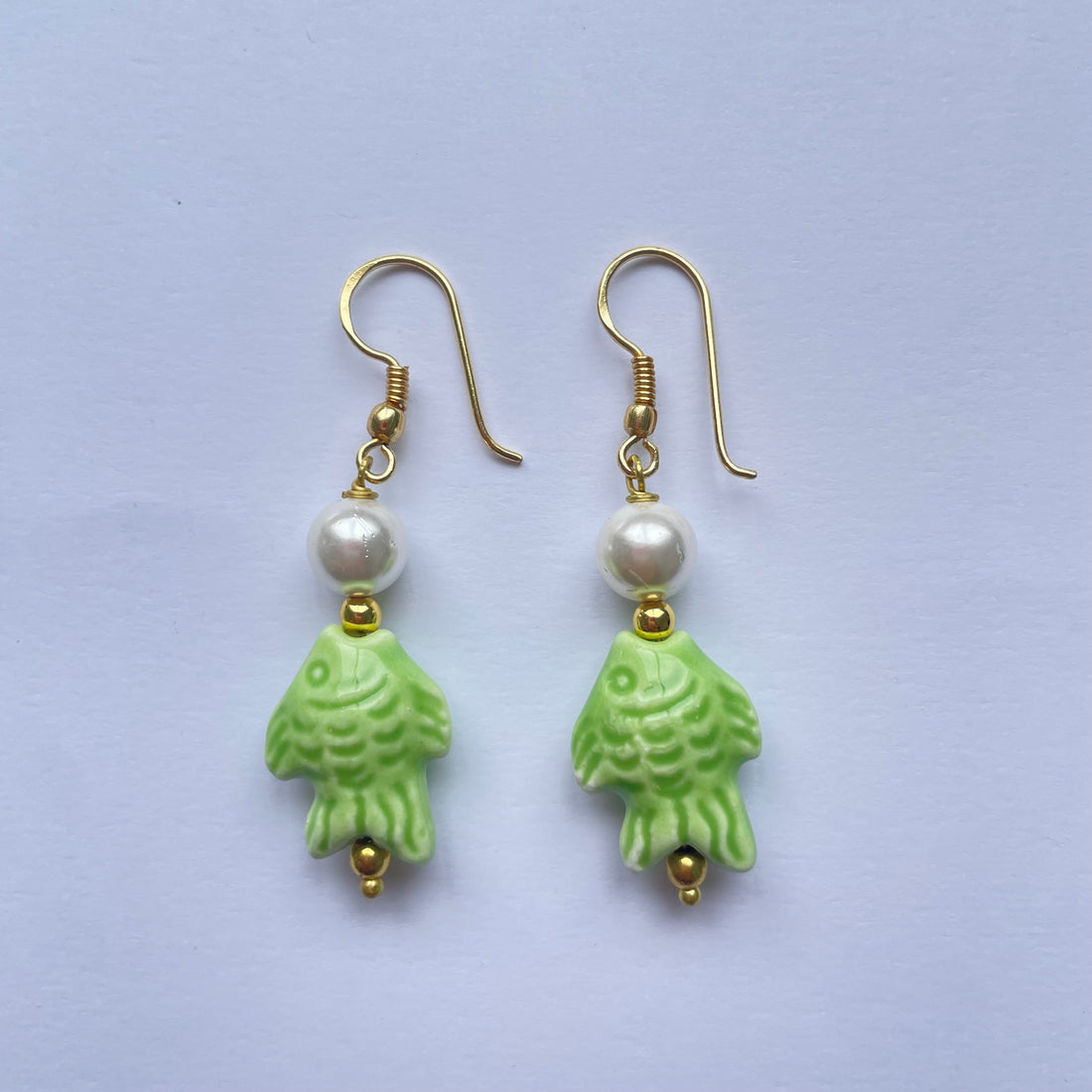 Pendientes cortos con pez de cerámica siciliana verde claro y adornado con una perla, el gancho es dorado y son de Marardi.