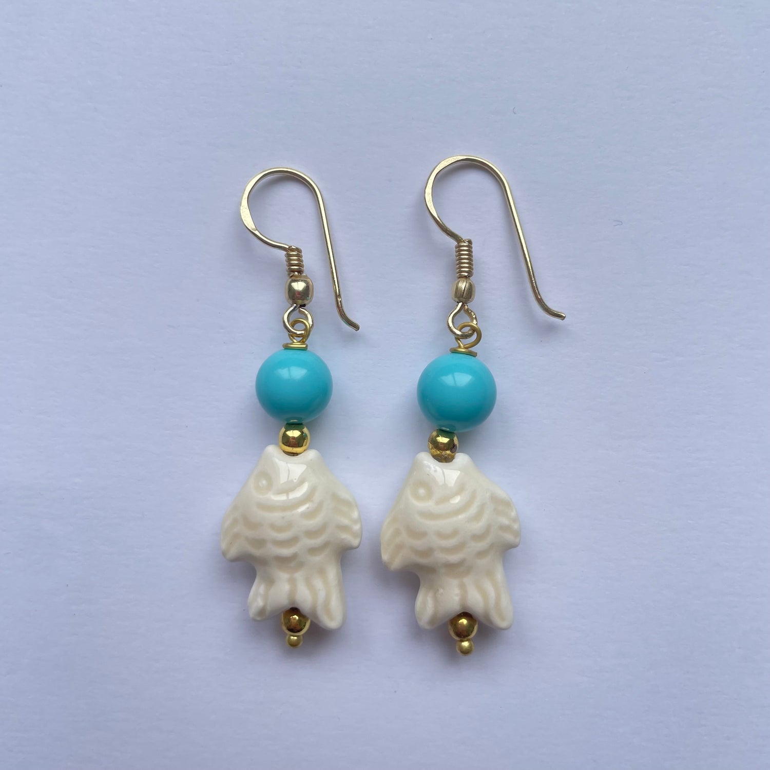 Pendientes cortos con pez de cerámica siciliana blanco adornado con una cuenta turquesa, el gancho es dorado y son de Marardi.