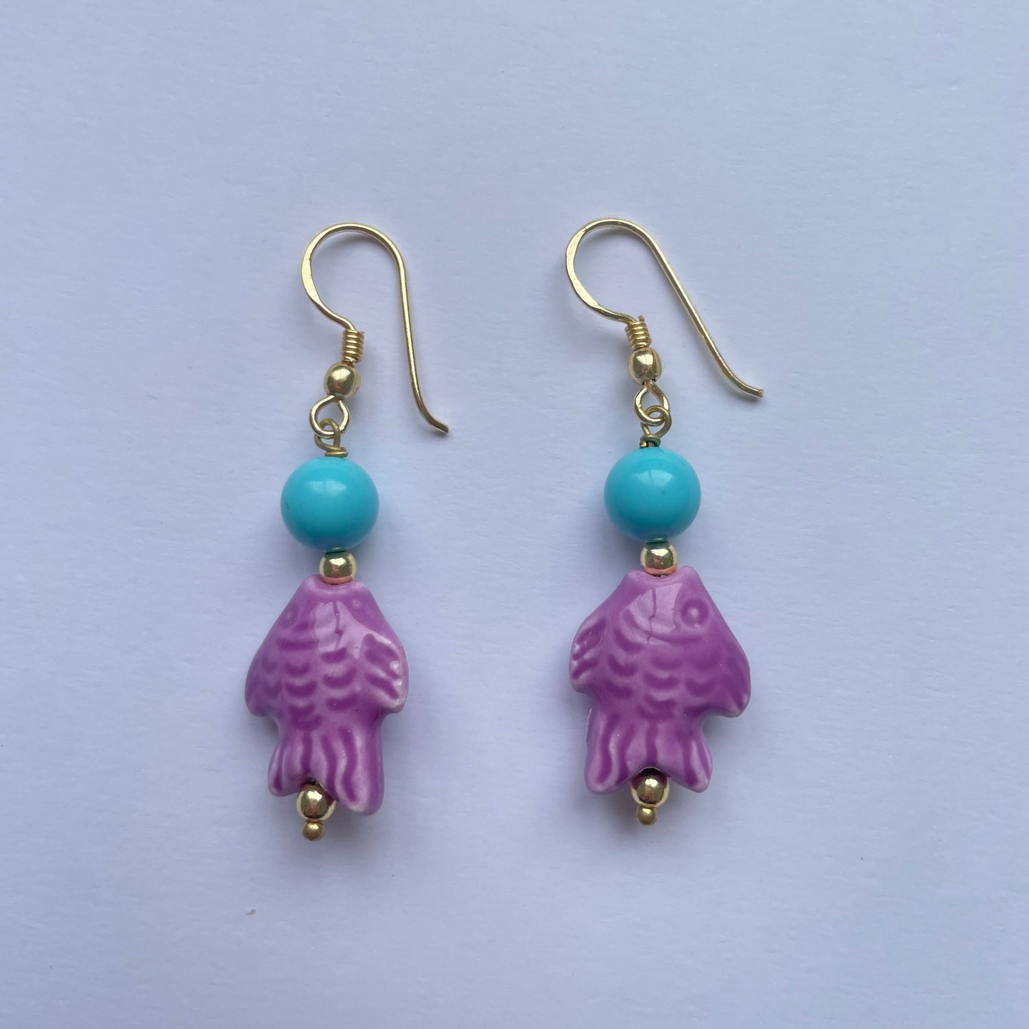 Pendientes cortos con pez de cerámica siciliana lila adornado con una cuenta turquesa, el gancho es dorado y son de Marardi.
