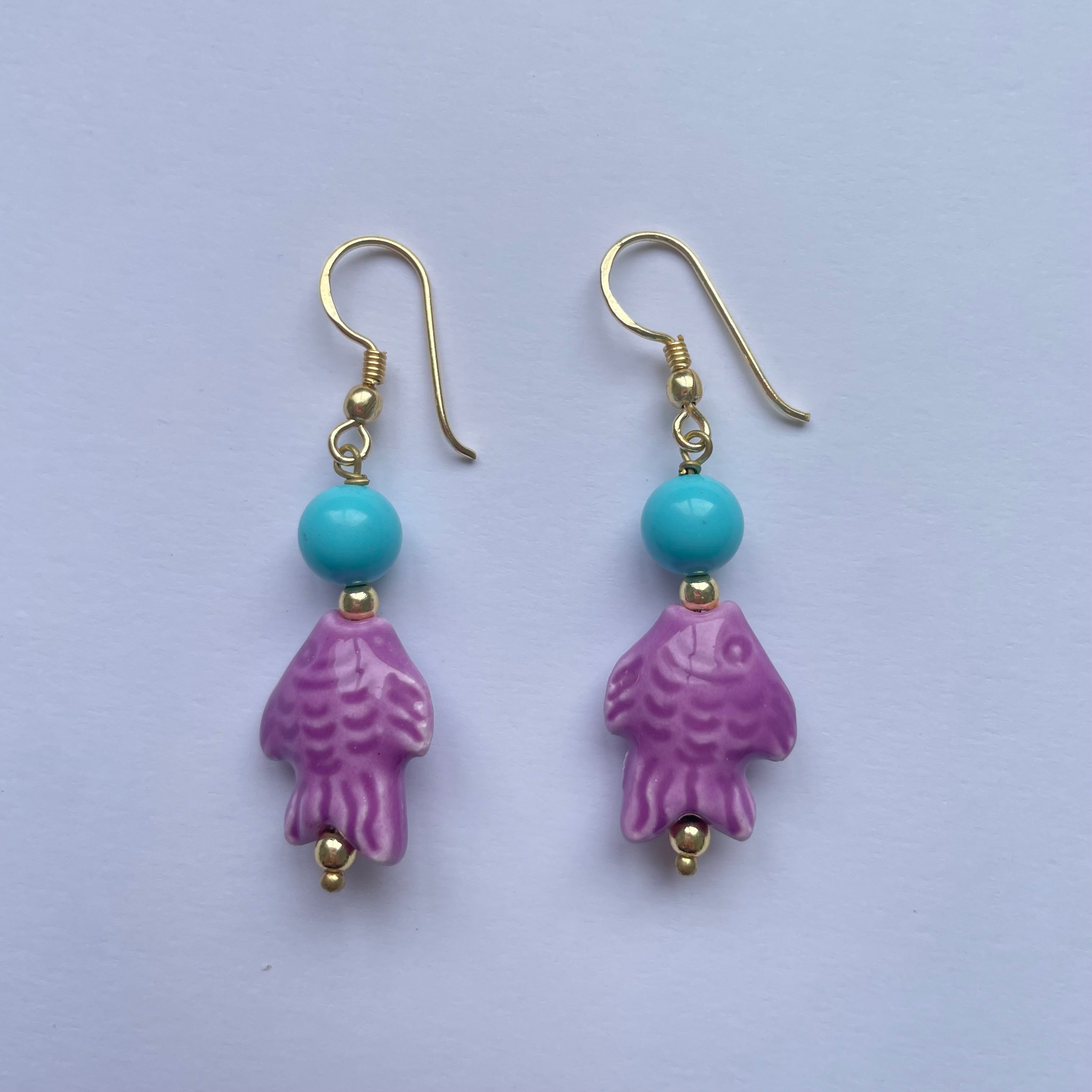 Pendientes cortos con pez de cerámica siciliana lila adornado con una cuenta turquesa, el gancho es dorado y son de Marardi.