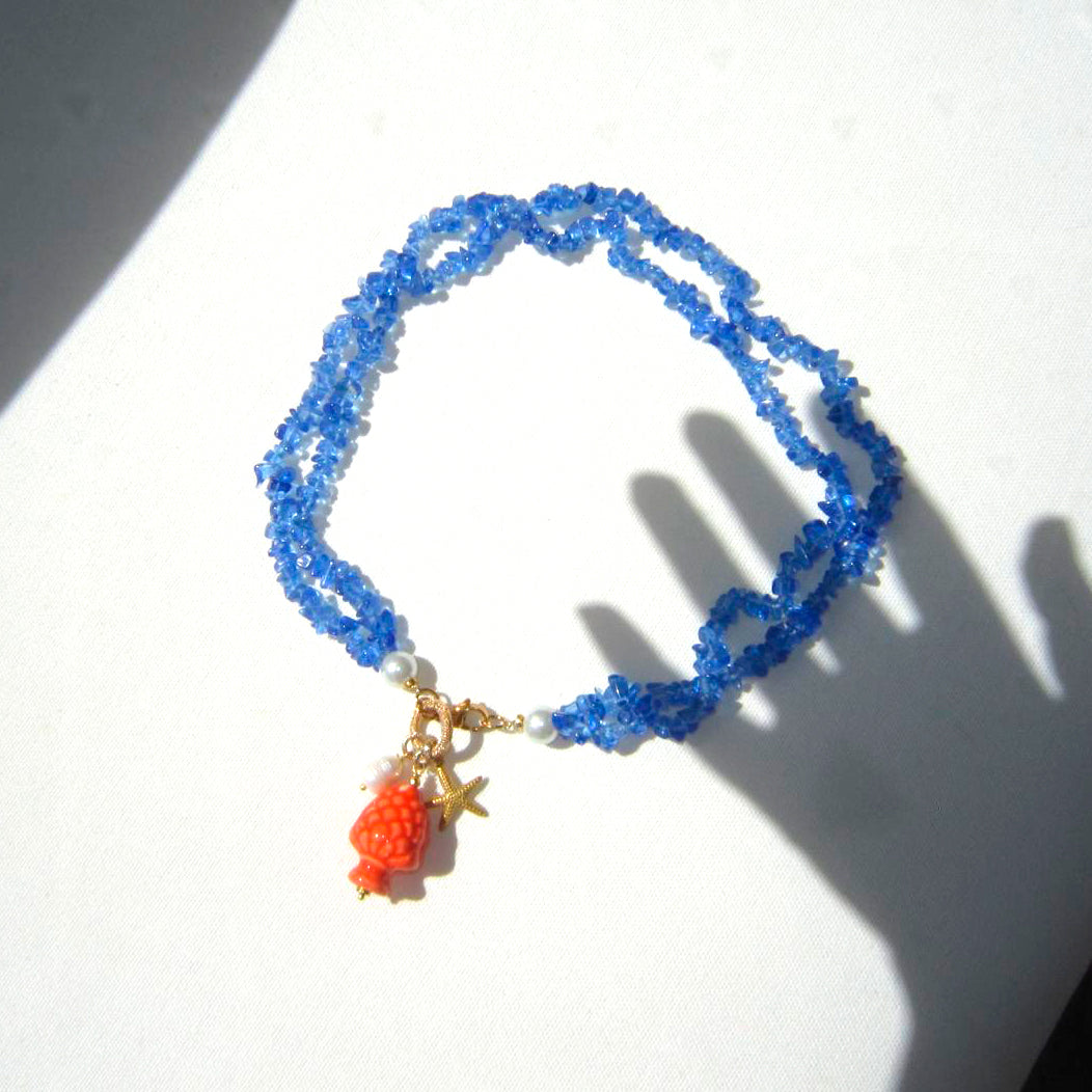 Collar corto de piedras azules y colgante de cerámica que es una piña naranja con una perla natural y estrella de marardi